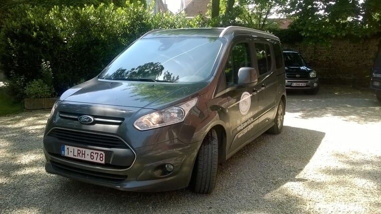 Véhicule gris Silly-Service du CPAS, floqué du logo, stationné devant une haie