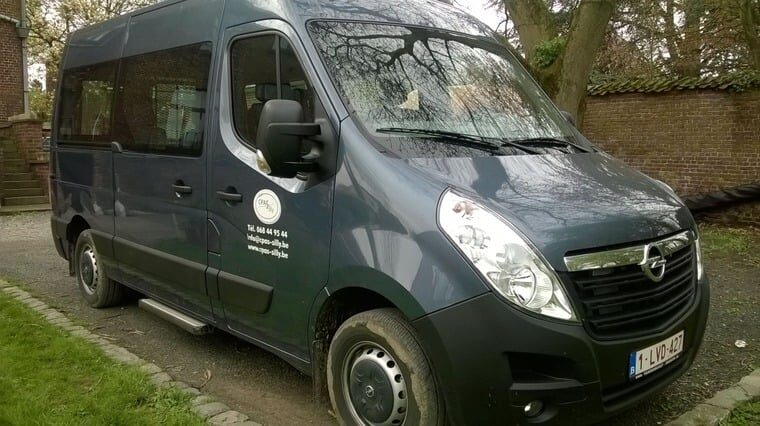 Minibus bleu nuit du CPAS adapté au transport PMR, garé le long d'un trottoir