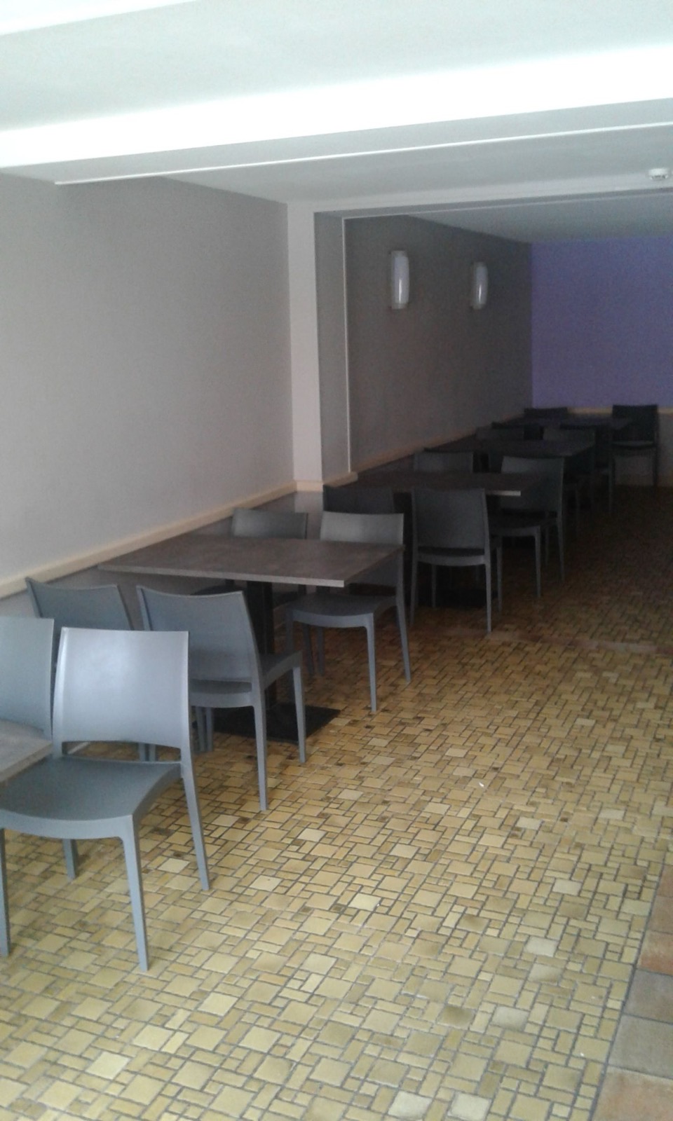 Salle du café du Salon de Graty : tables et chaises grises sur un sol en mosaïque ocre