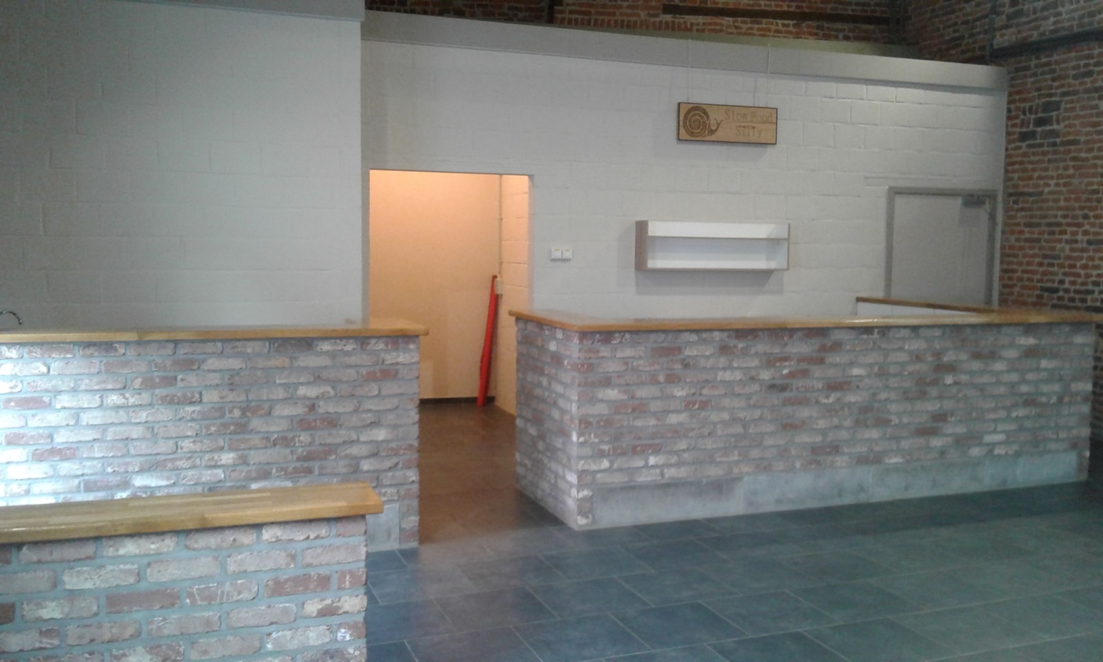 Espace bar de la grande salle du Salon de Graty avec comptoir en briques et panneau Slow Food Silly