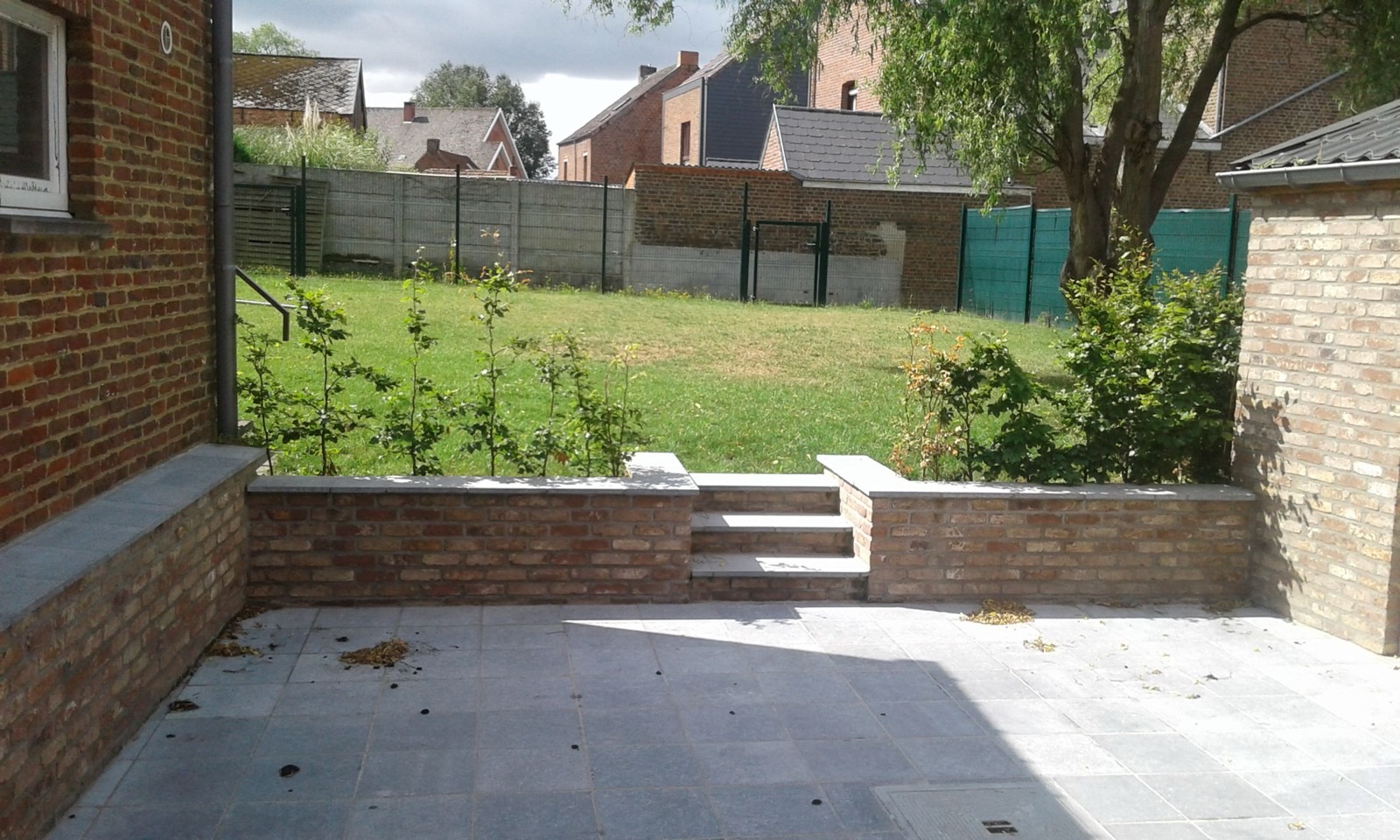 Terrasse extérieure pavée et sécurisée de la grande salle, donnant sur un jardin clôturé