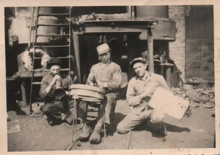 Photo ancienne en noir et blanc : trois ouvriers posent dans un atelier