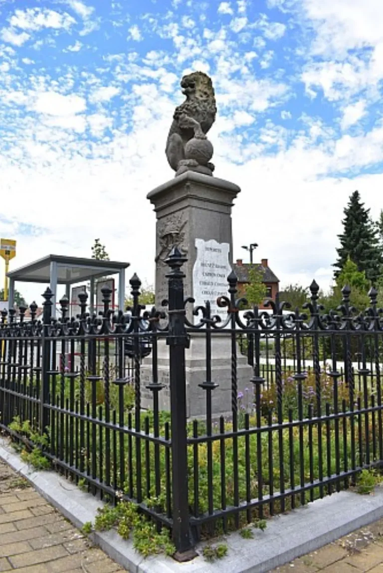 Monument aux morts surmonté d'un lion, entouré d'une grille en fer forgé