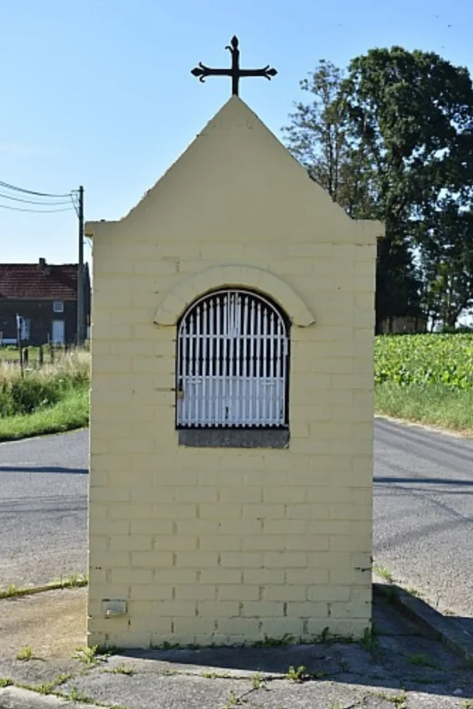 Chapelle jaune au toit pointu surmonté d'une croix, au bord d'une route