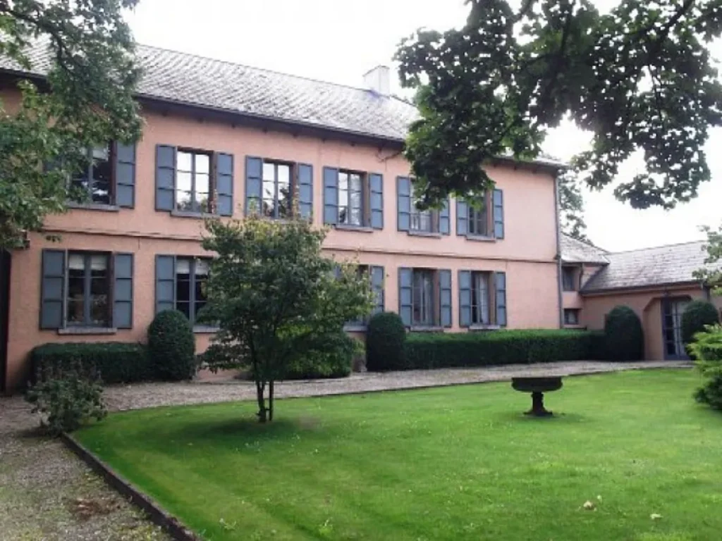 Façade rose d'une demeure aux volets gris-bleu, devant une pelouse
