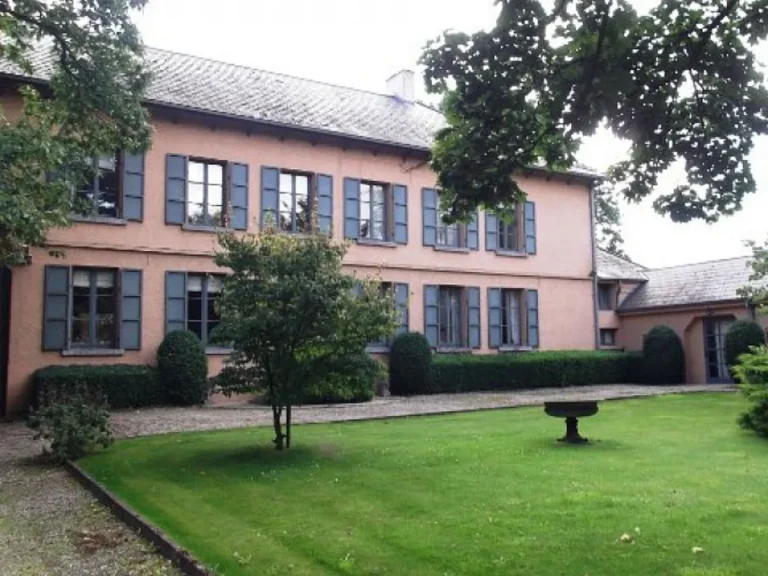 Façade rose d'une demeure aux volets gris-bleu, devant une pelouse