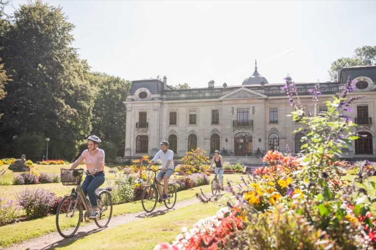 Cyclistes sur une allée des jardins fleuris, devant un château blanc