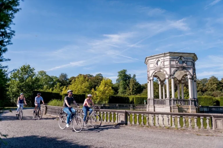 Quatre cyclistes le long d'une balustrade de pierre, près d'un kiosque à colonnes