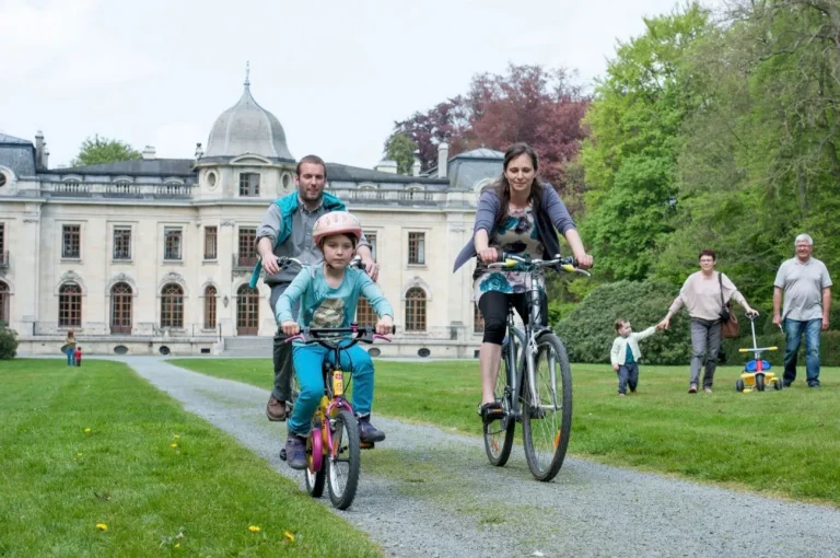 Famille à vélo sur une allée de parc, devant un château à dôme