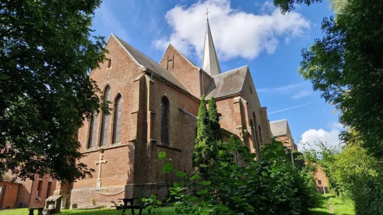 Église de briques rouges au clocher pointu, vue depuis la pelouse qui la borde