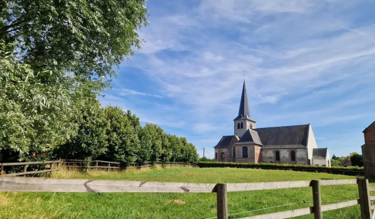 Église au clocher pointu vue au-delà d'une prairie clôturée