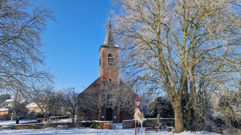 Église au clocher pointu et arbres givrés, sur une place enneigée