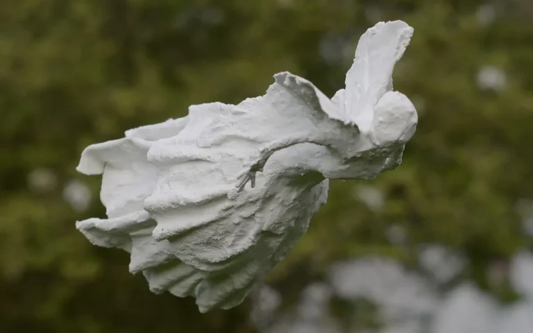 Sculpture blanche d'une fée aux ailes déployées, devant un feuillage