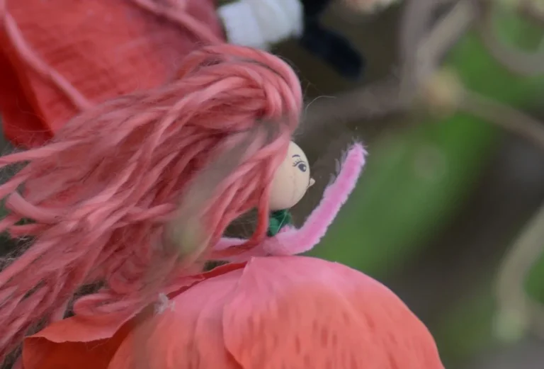 Poupée de fée aux cheveux de laine rose posée sur une fleur rouge