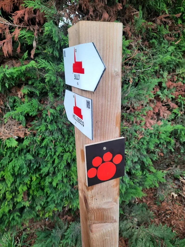 Poteau de balisage en bois avec deux flèches directionnelles et la plaquette à patte rouge du Circuit Toutous