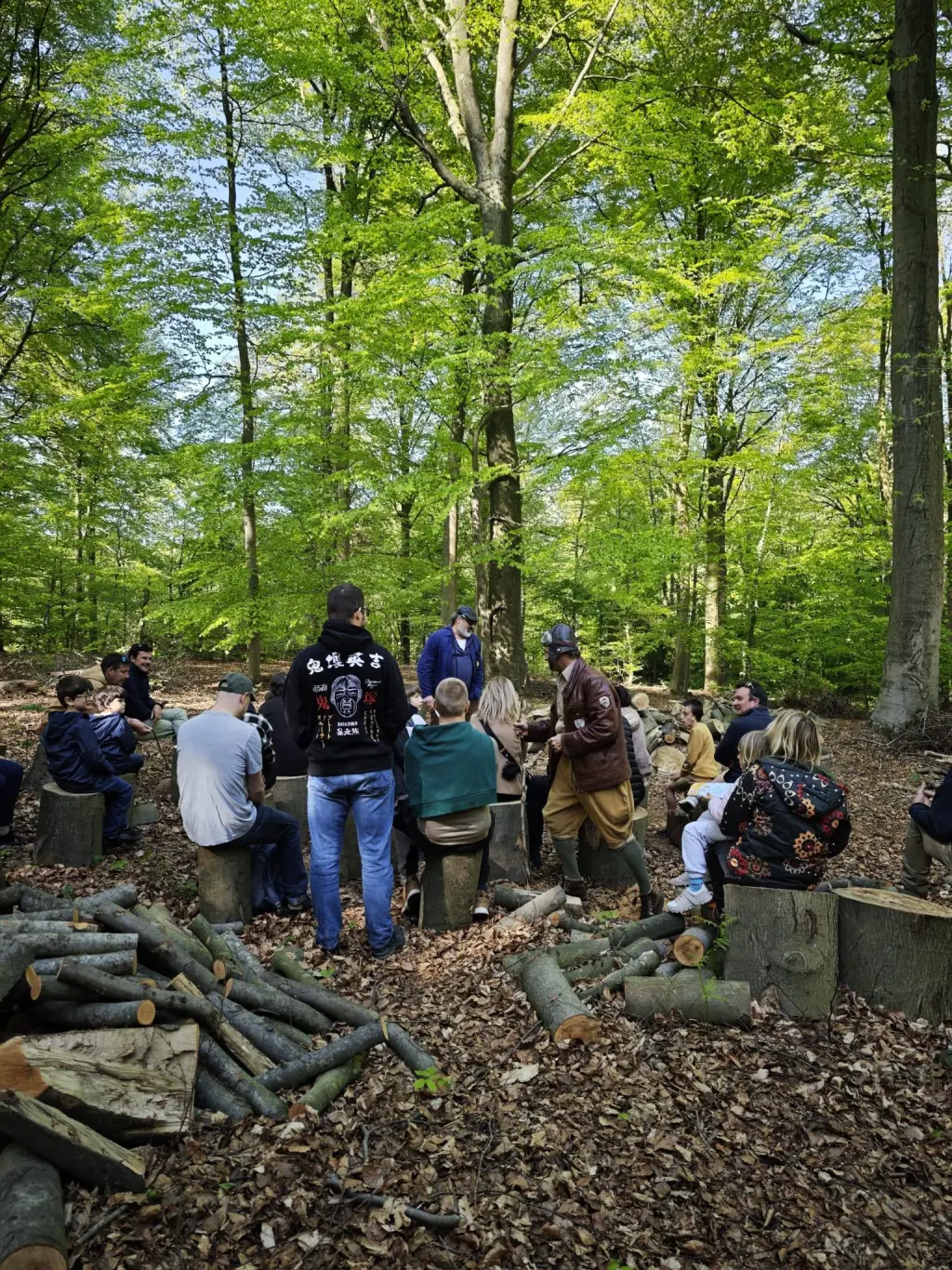 Groupe de visiteurs réunis en forêt autour d'un guide, assis sur des rondins, lors d'une animation MaquiStory à Saint-Marcoult