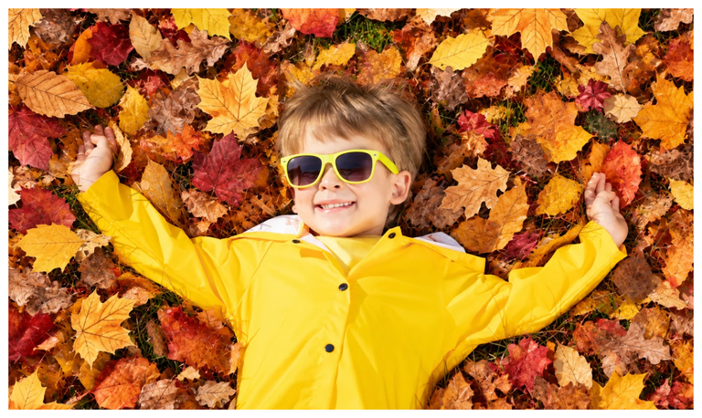 Enfant en ciré jaune et lunettes de soleil, allongé dans les feuilles mortes