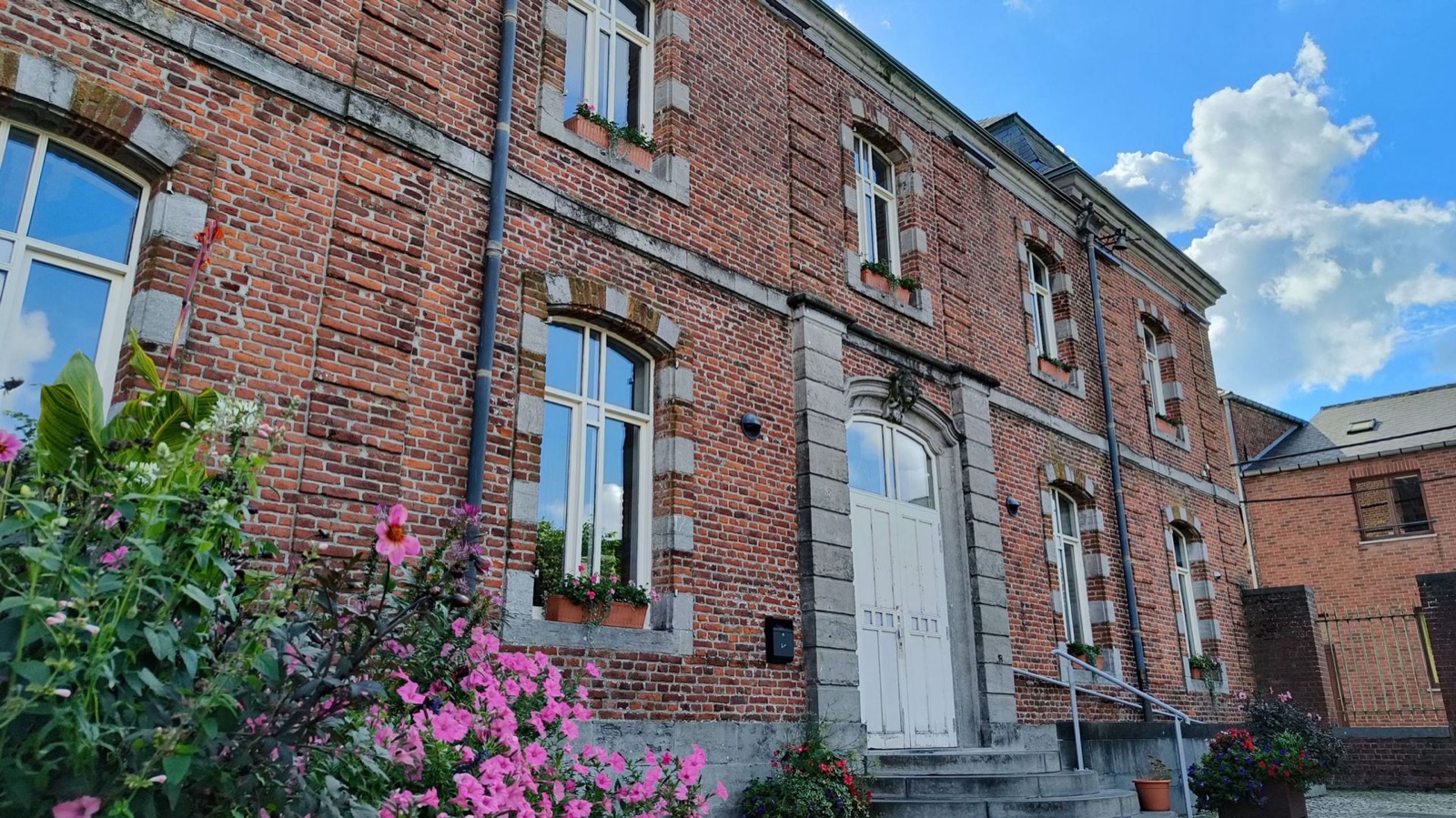 Bâtiment communal de Silly en briques rouges aux encadrements de pierre, fleuri de géraniums et de fleurs roses