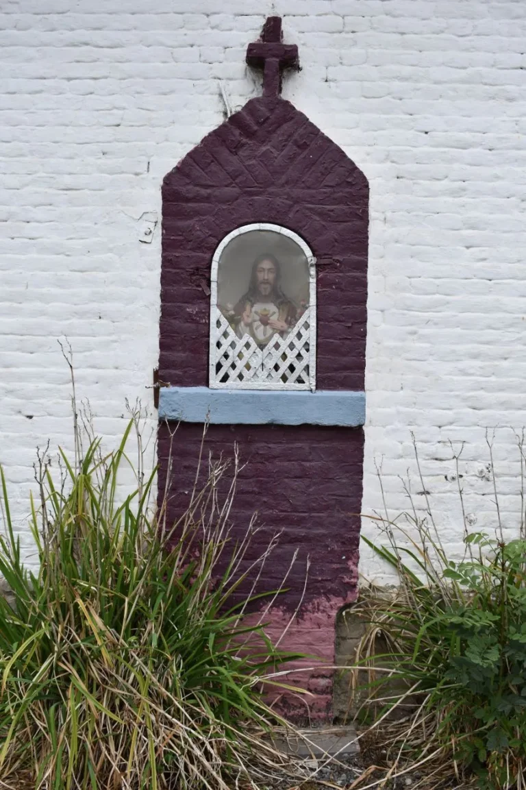 Potale peinte en violet contre un mur blanchi, image du Sacré-Cœur derrière une grille ajourée et reposoir bleu clair