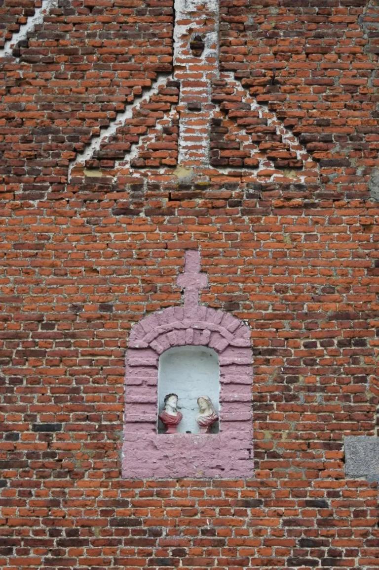 Niche cintrée au contour peint, surmontée d'une croix, dans un pignon de briques, abritant les bustes de Jésus et de Marie