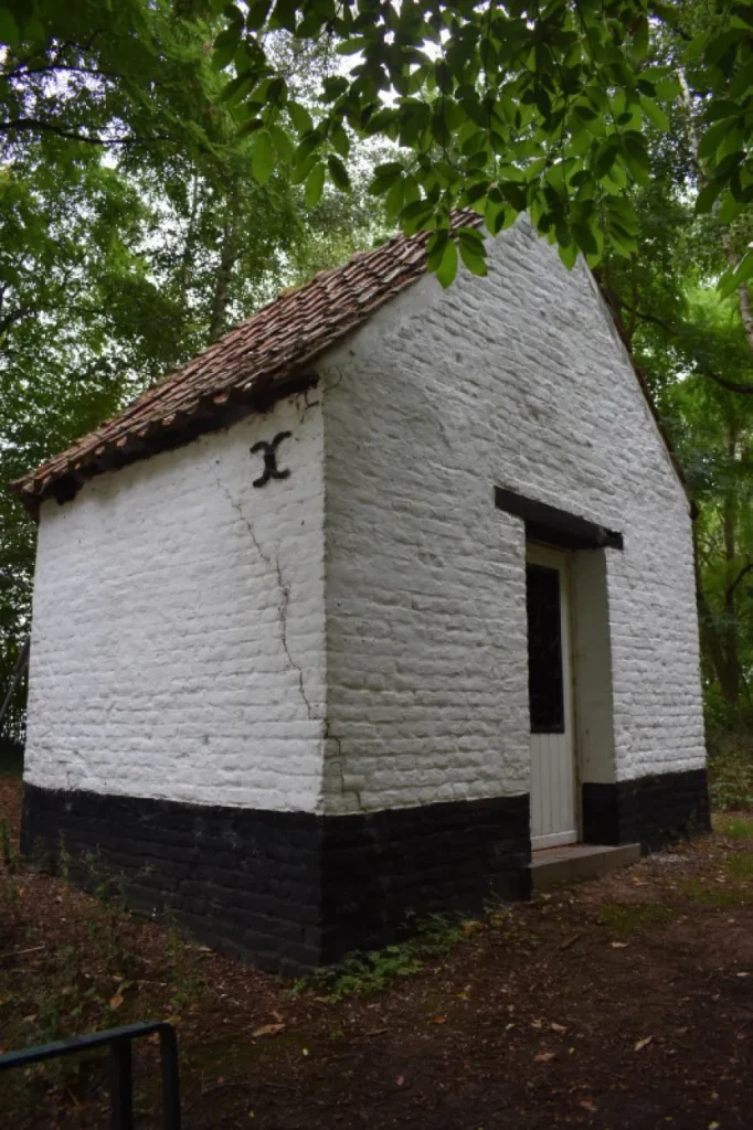 Chapelle en briques blanchies à soubassement noir, toit de tuiles et porte blanche, sous les arbres