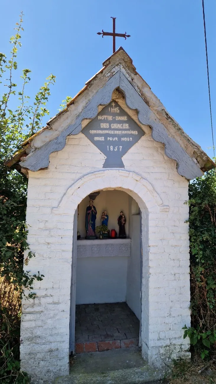 Petite chapelle blanchie coiffée d'une croix en fer, plaque en losange « Notre-Dame des Grâces, 1857 » au-dessus de l'entrée et statues sur l'autel