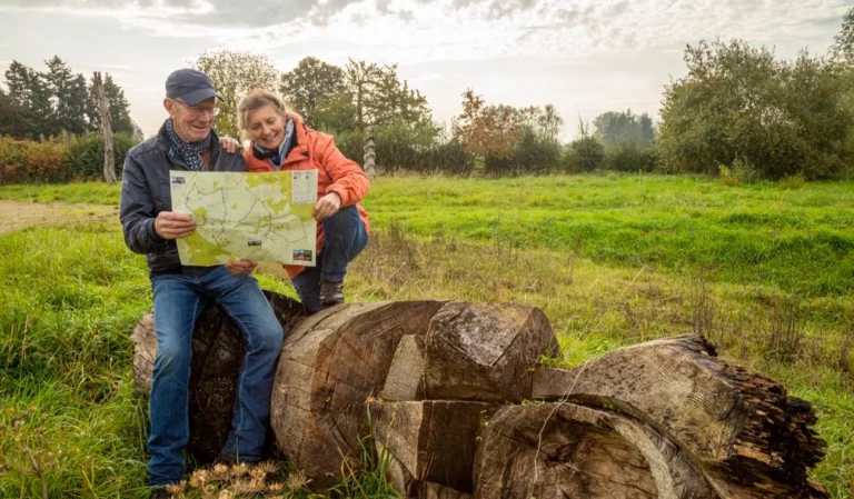 Couple de promeneurs assis sur des troncs, qui consulte une carte au bord d'une prairie