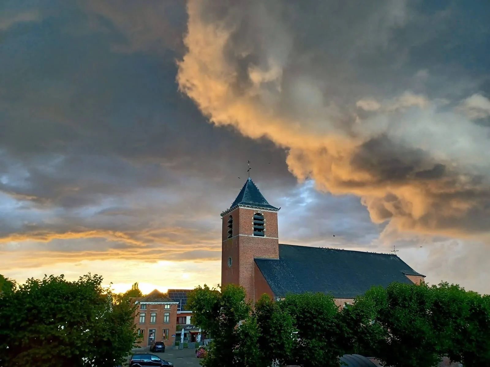 Clocher en briques d'une église de Silly se détachant sur un ciel de coucher de soleil aux nuages orangés