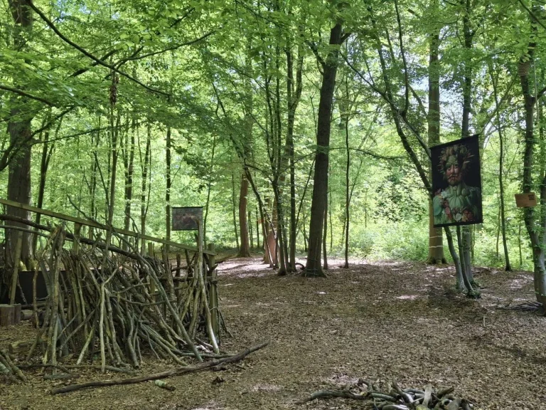 Clairière du bois avec une cabane de branchages et la reproduction d'un portrait d'Arcimboldo suspendue à un arbre