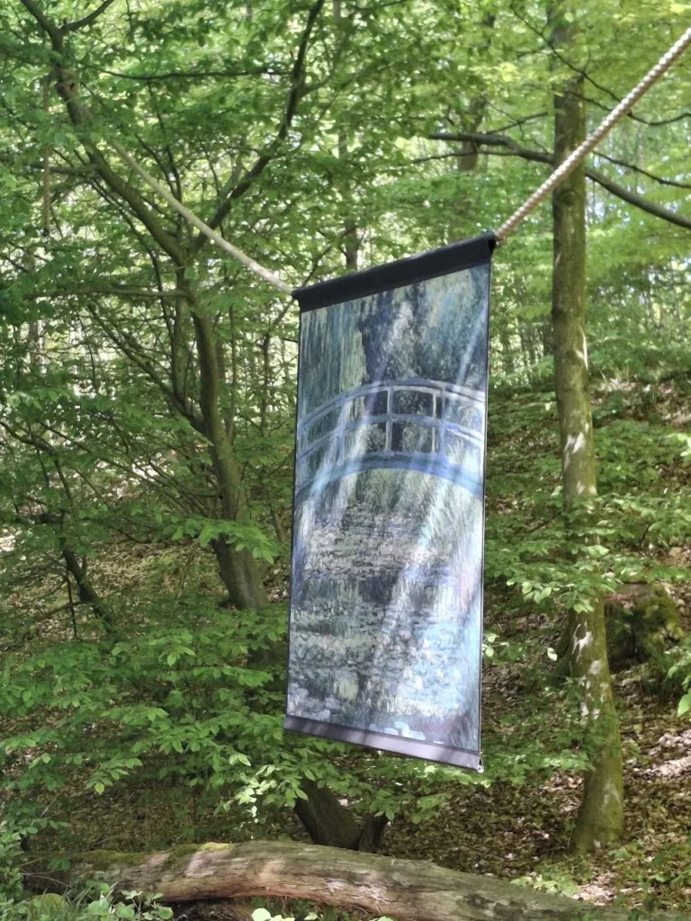 Reproduction d'un tableau de Monet, un pont japonais sur un étang, suspendue à une corde entre les arbres