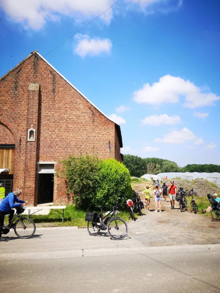 Cyclistes devant une grange en briques et des serres, sur le circuit des maraîchers