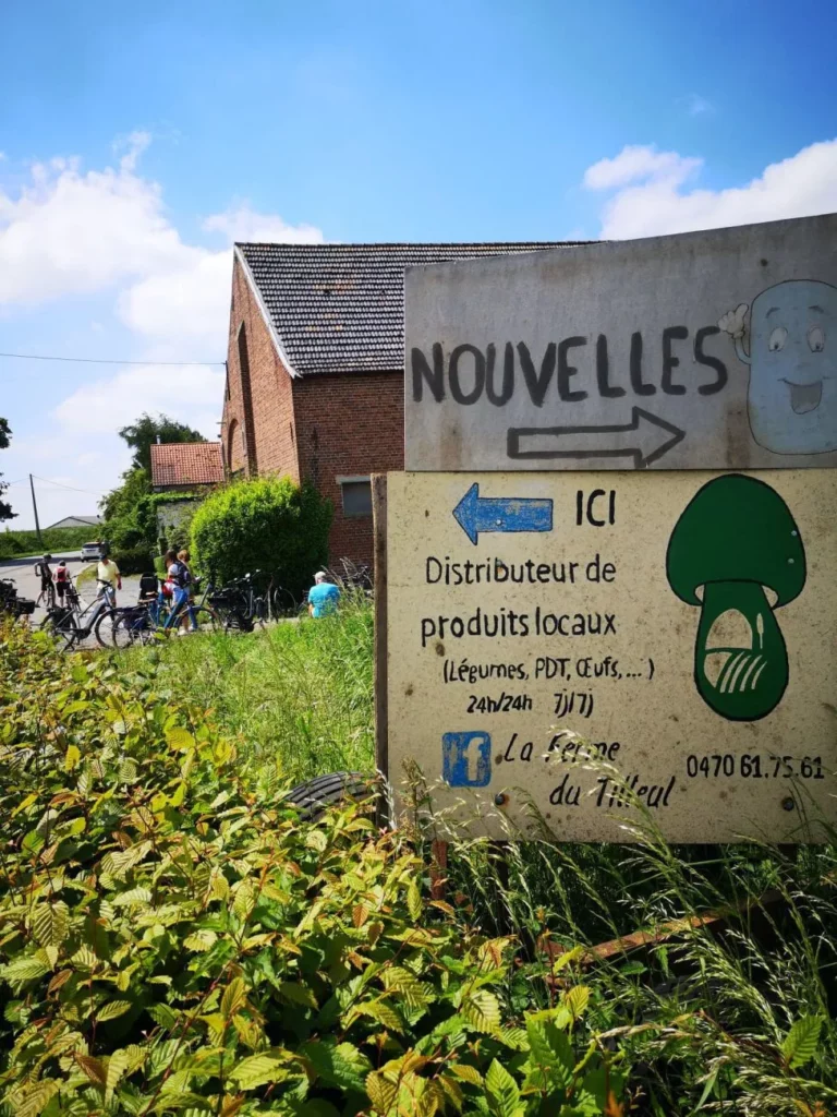 Panneau « Distributeur de produits locaux » de la Ferme du Tilleul, devant une ferme en briques