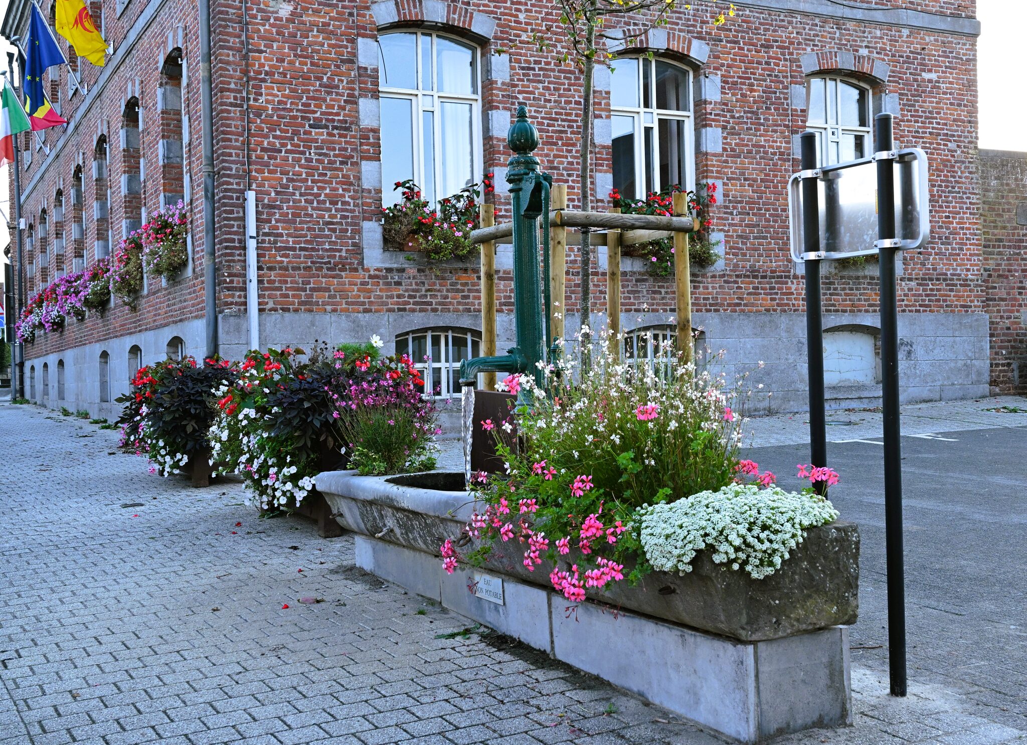 Abreuvoir en pierre fleuri et pompe en fonte devant la façade de la Maison communale de Silly