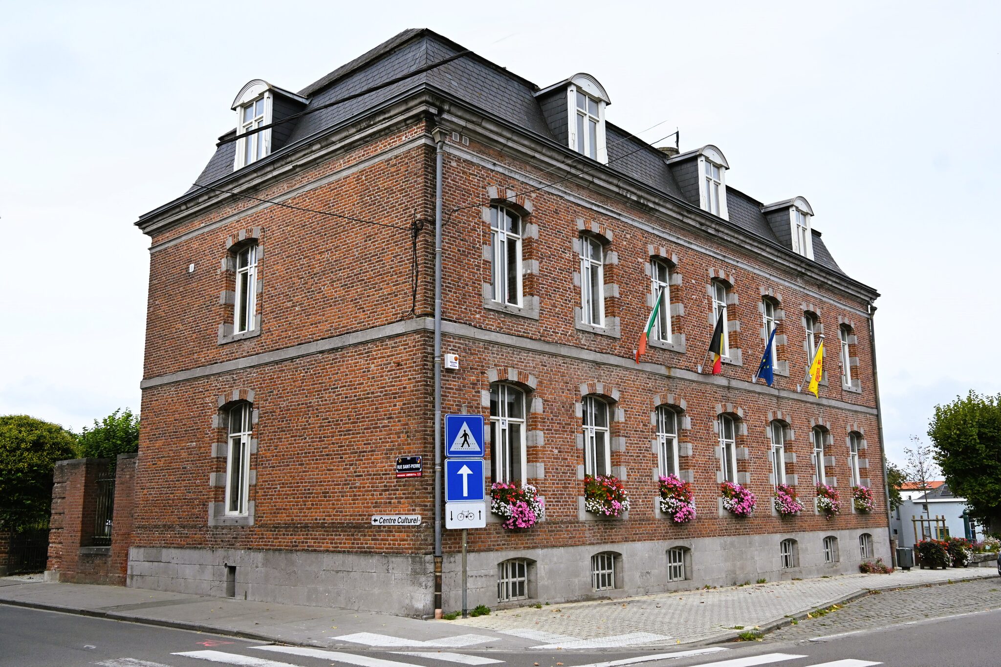 Maison communale de Silly à l’angle de la rue Saint-Pierre : façade en briques, drapeaux et fenêtres fleuries