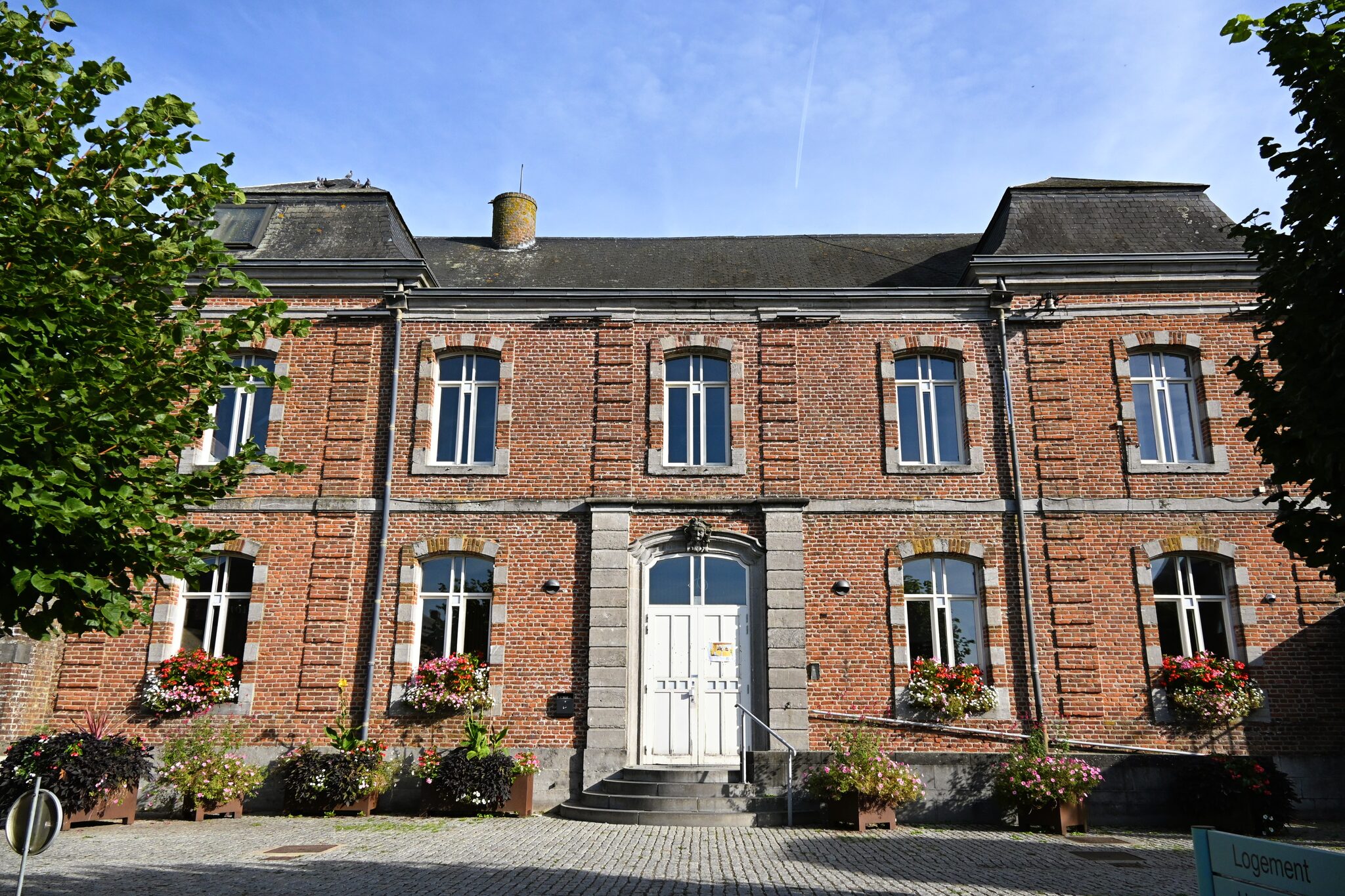 Maison communale de Silly sous un ciel bleu : façade en briques à encadrements de pierre, porte blanche et jardinières fleuries