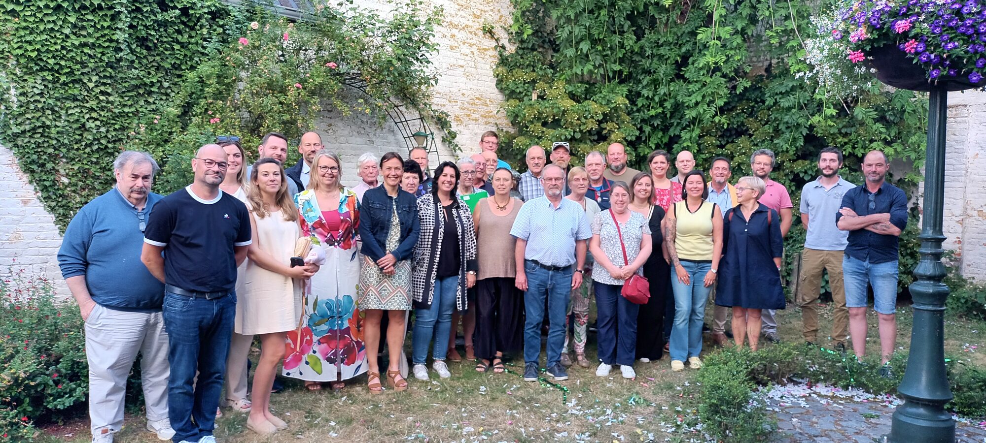 Une quarantaine de membres de la CLDR de Silly réunis pour une photo de groupe dans un jardin, devant un mur de briques couvert de lierre et de rosiers grimpants.